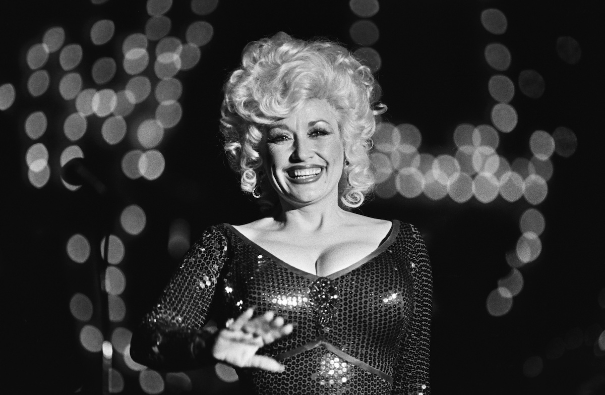 Dolly Parton fekete fehér felvételen, csillogó felsőben és göndör hajjal