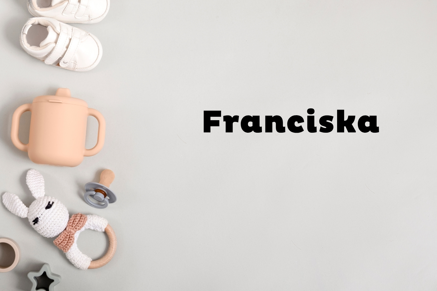 Franciska | Marie Claire Szürke háttéren oldalt fehér babacipő, rózsaszín ivópohár, cumi és csörgő