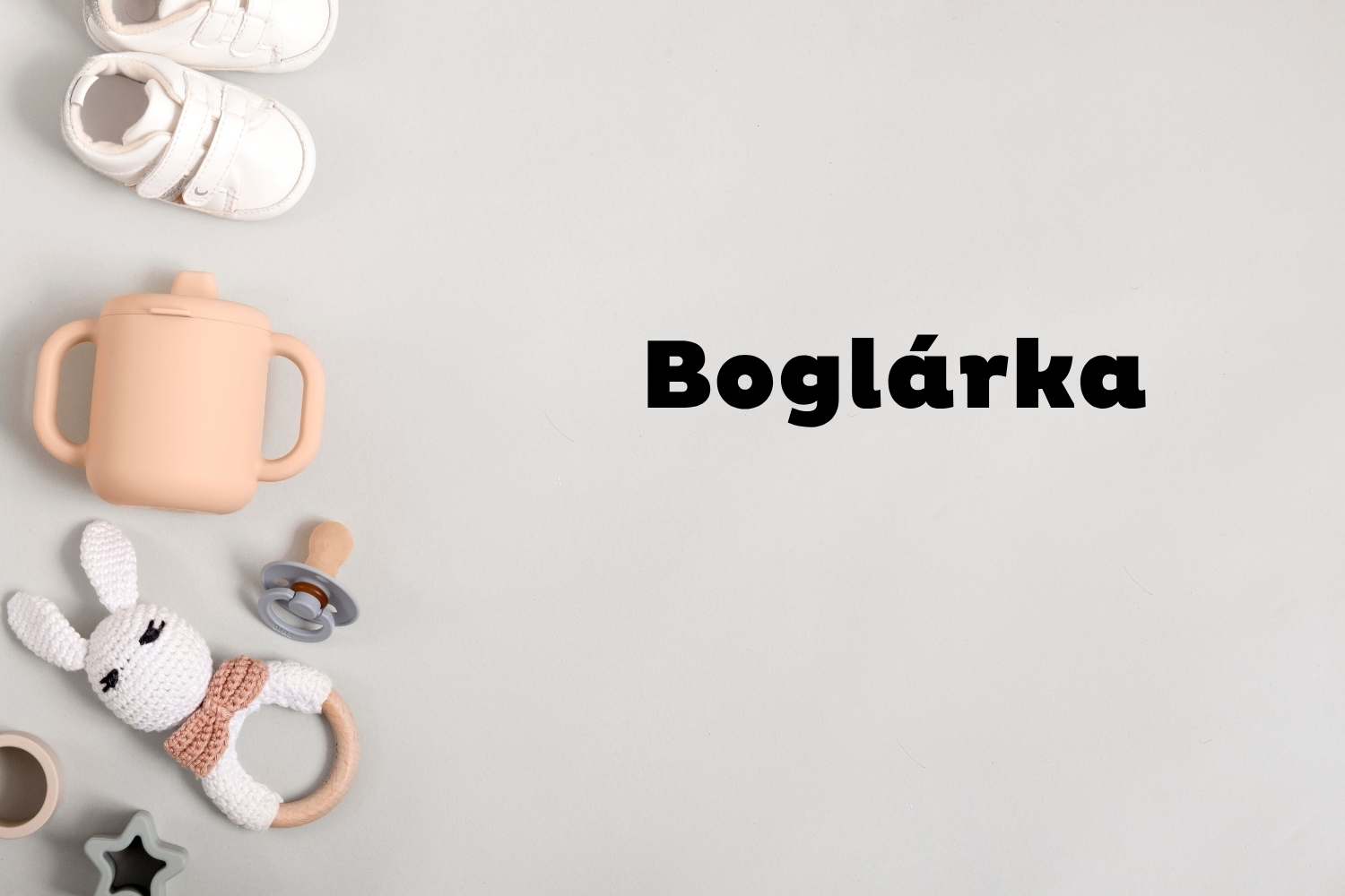 Boglárka | Marie Claire Szürke háttéren oldalt fehér babacipő, rózsaszín ivópohár, cumi és csörgő