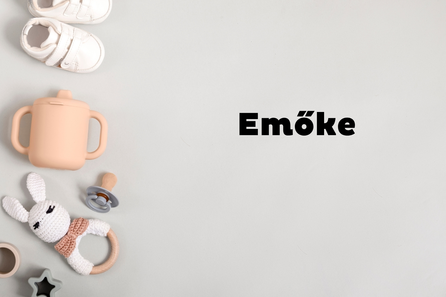 Emőke | Marie Claire Szürke háttéren oldalt fehér babacipő, rózsaszín ivópohár, cumi és csörgő