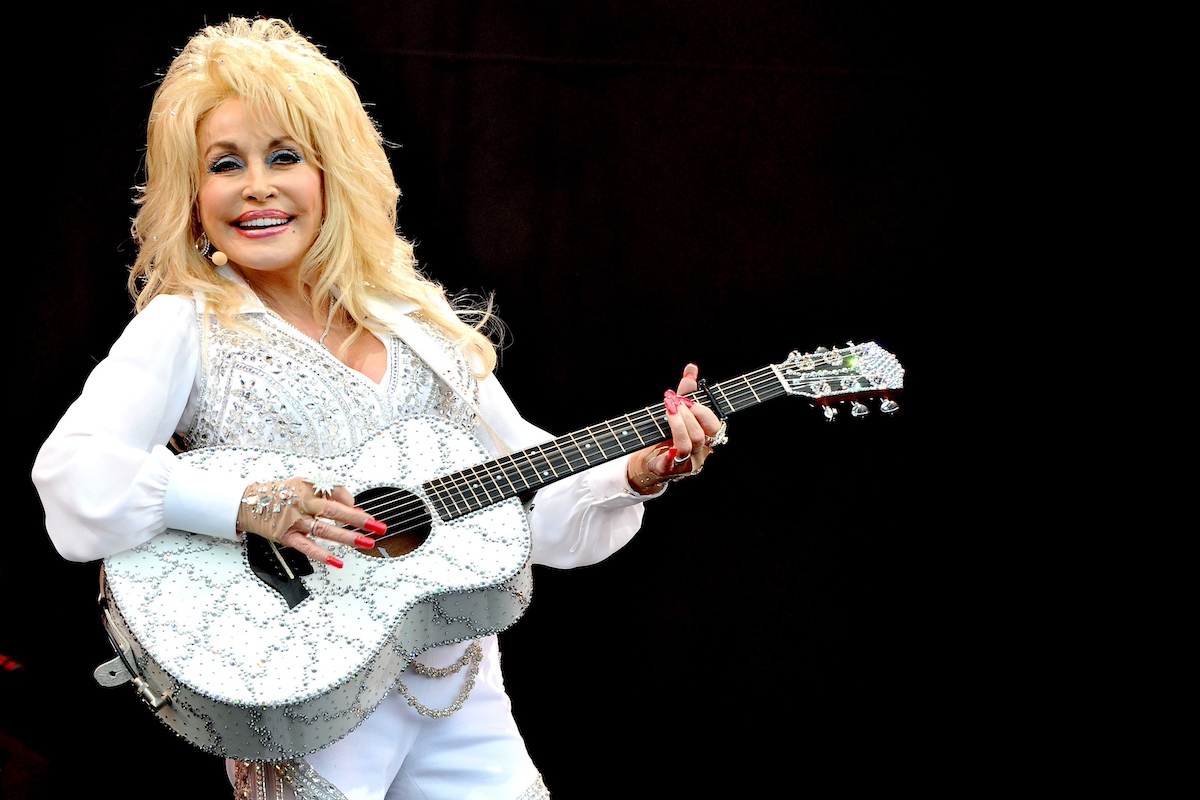 Dolly Parton fekete háttér előtt, gitárral