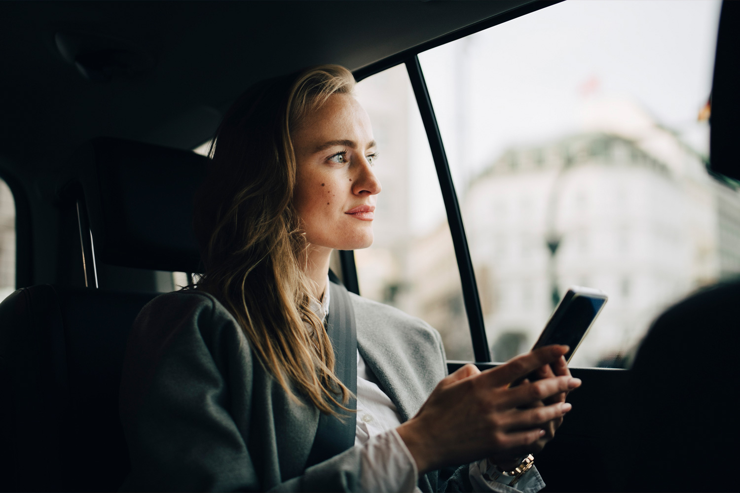 Egy mosolygó nő mobiltelefont tart a kezében