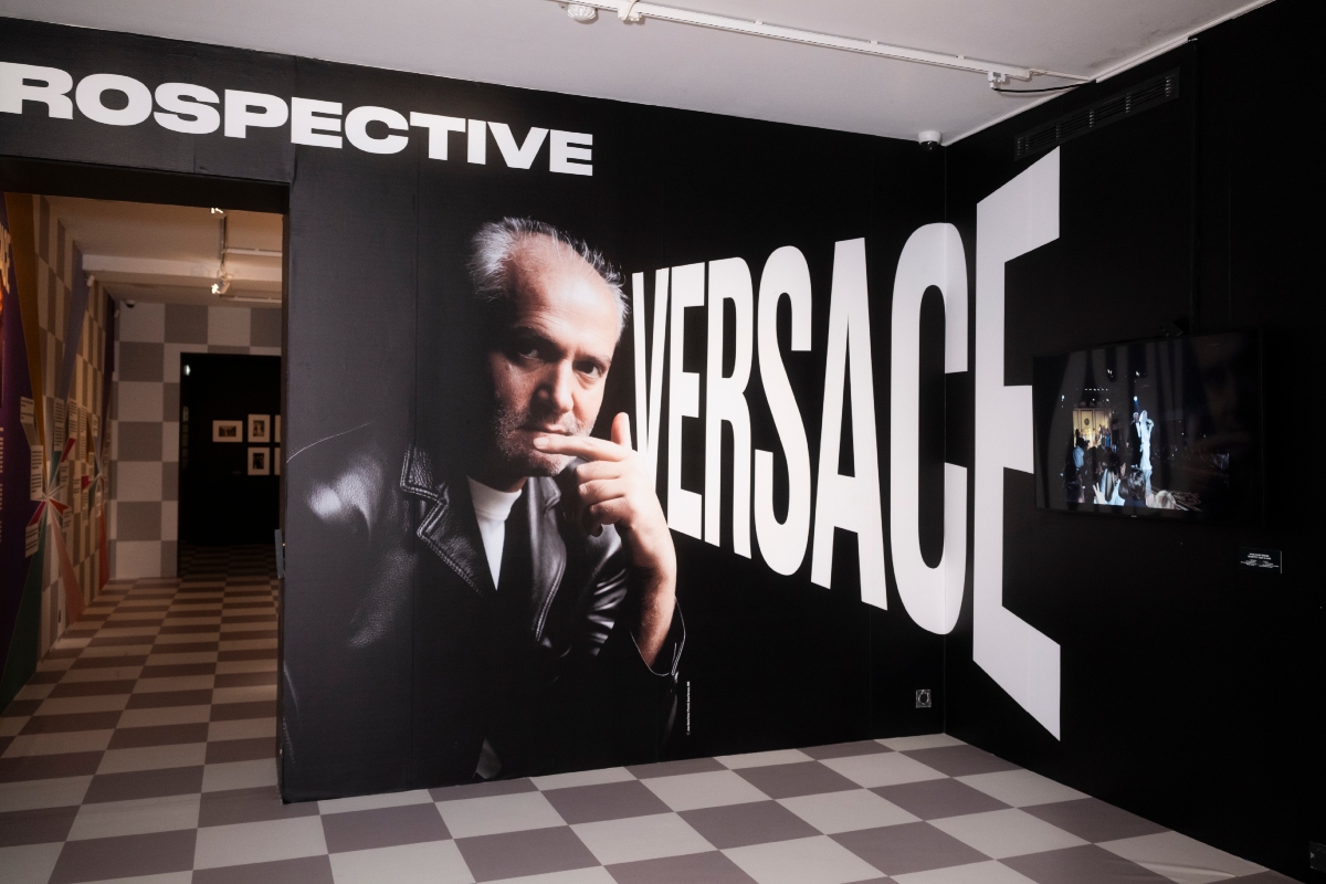 A kiállítás bejárata: Gianni Versace fekete-fehér portréja és a Versace felirat a falon.