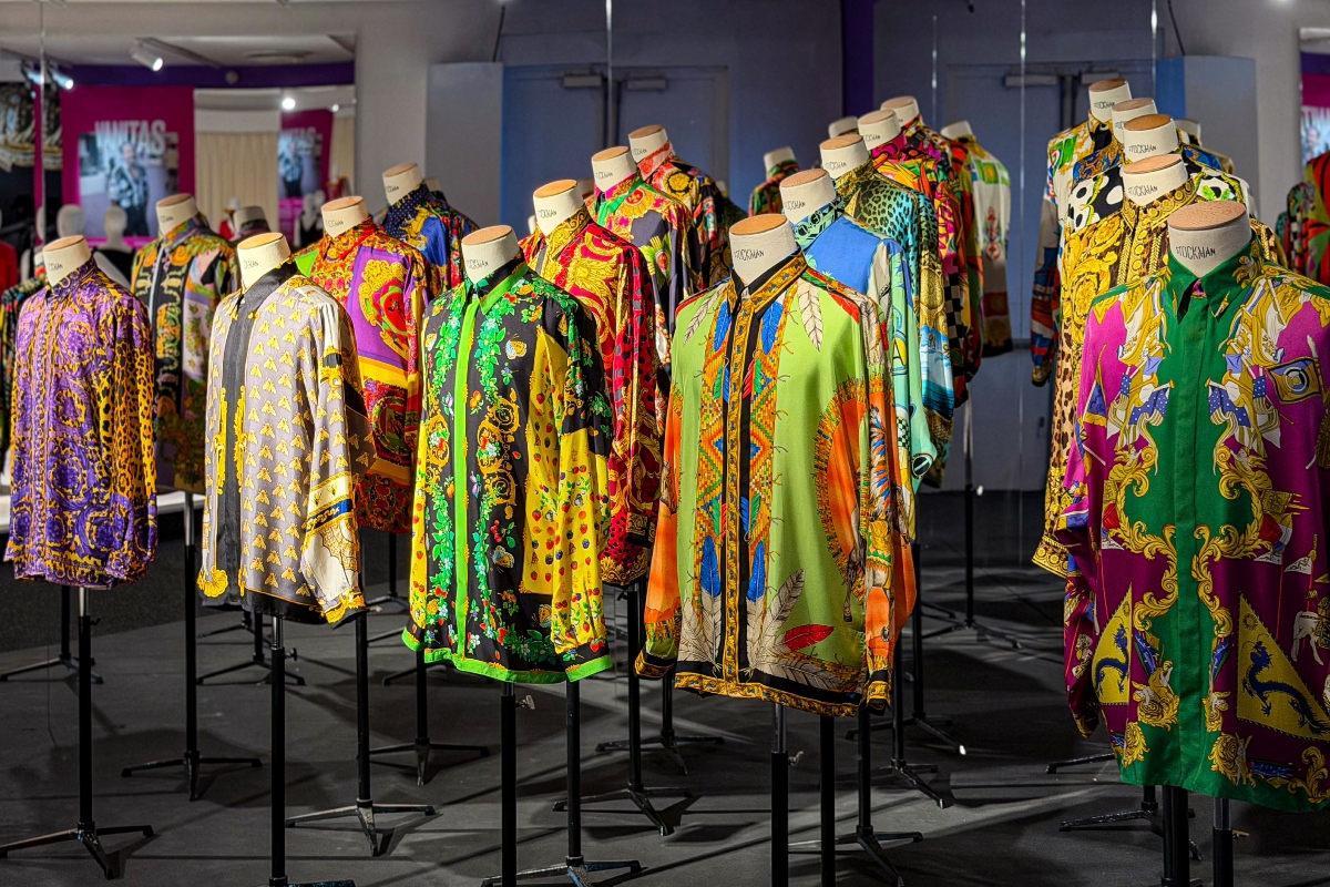 versace-retrospektiv-kiallitas-parizs-2026 | Marie Claire Élénk színű, mintás selyemingek bábukon, sűrű sorokban egy kiállítóteremben.