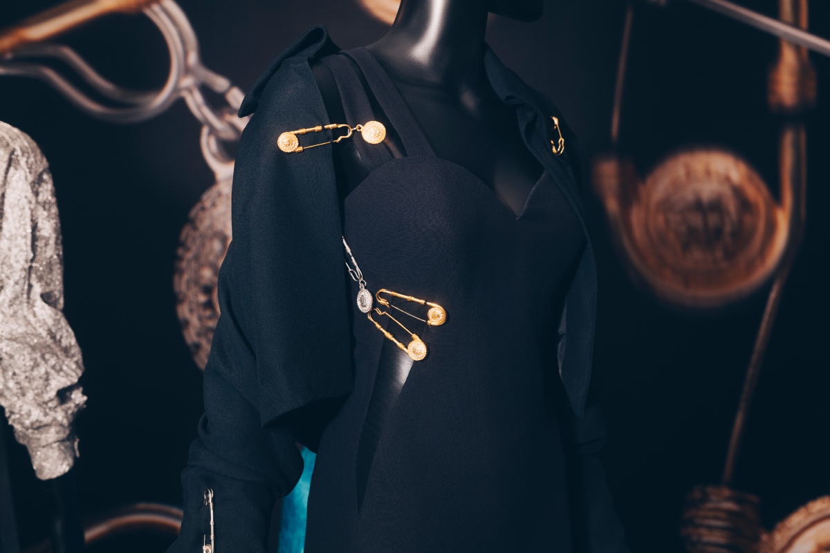 versace-retrospektiv-kiallitas-parizs-2026 | Marie Claire Fekete Versace-ruha közelről, aranyszínű, Medúza-fejes biztosítótűkkel összefogva.