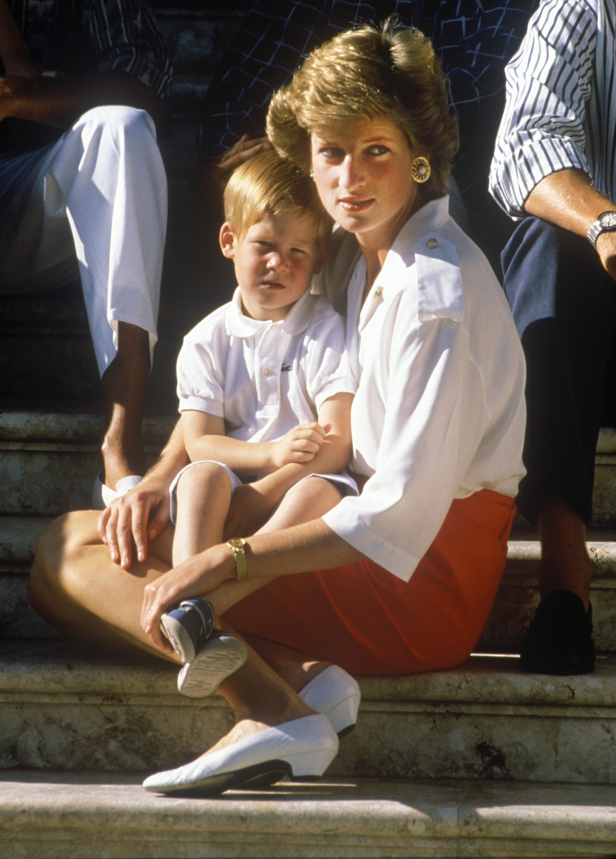 harry-herceg-neve-diana-karoly | Marie Claire Diana piros szoknyában guggol, az ölében a kis Harry herceg
