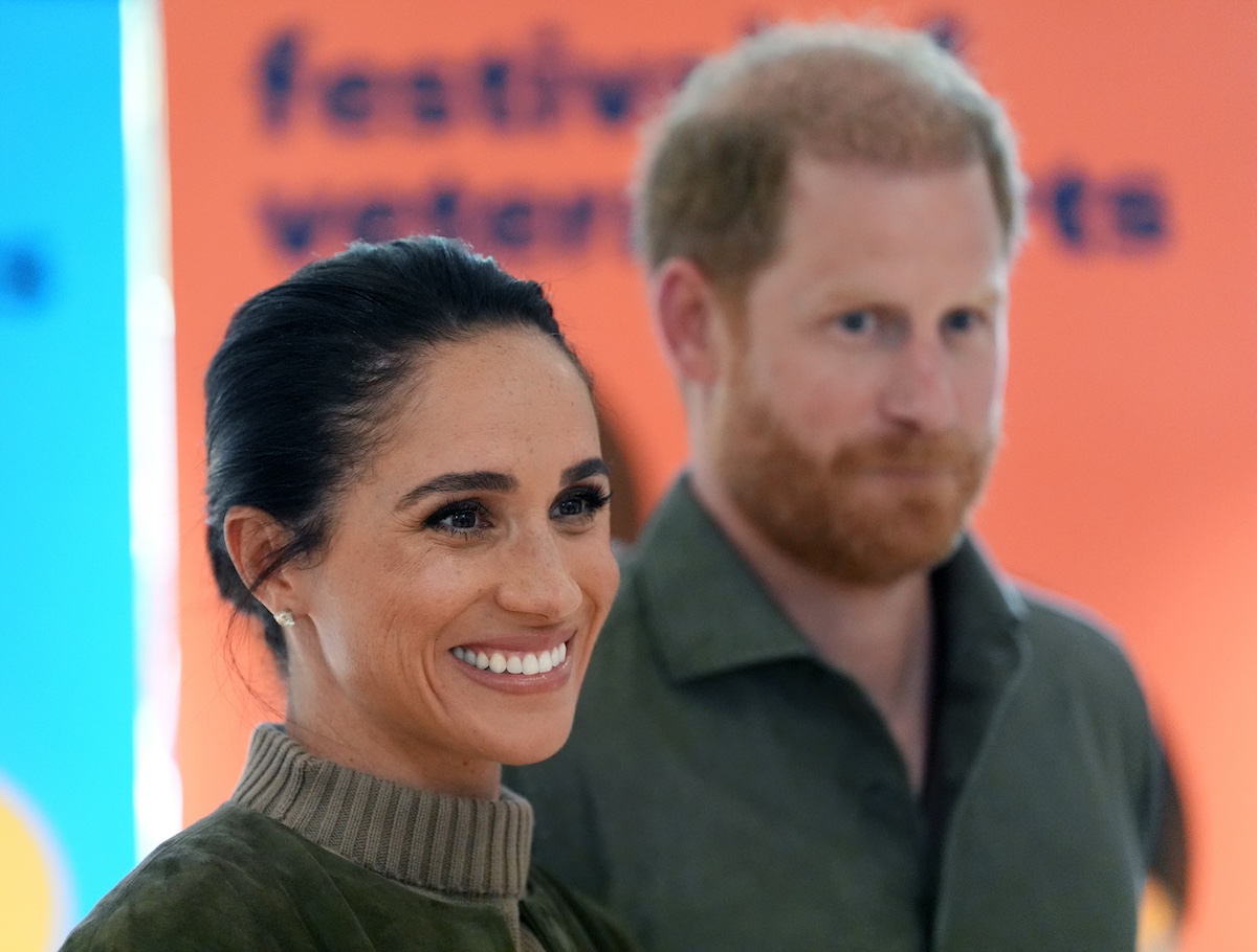 felhobor-sminktrend-40-felett | Marie Claire Meghan Markle zöld felsőben, közelről, a háttérben Harry hercge