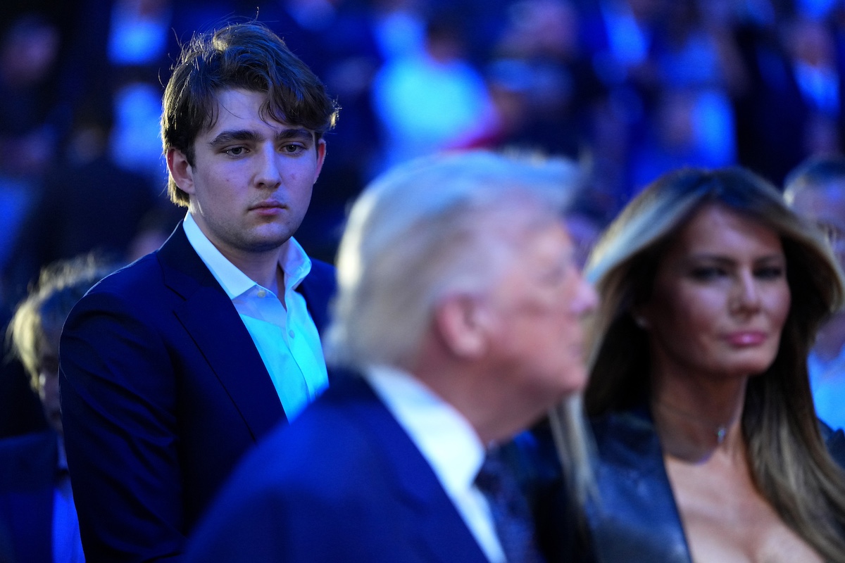 Barron Trump kék fényben, az előtérben, homályosan Donald és Melania Trump
