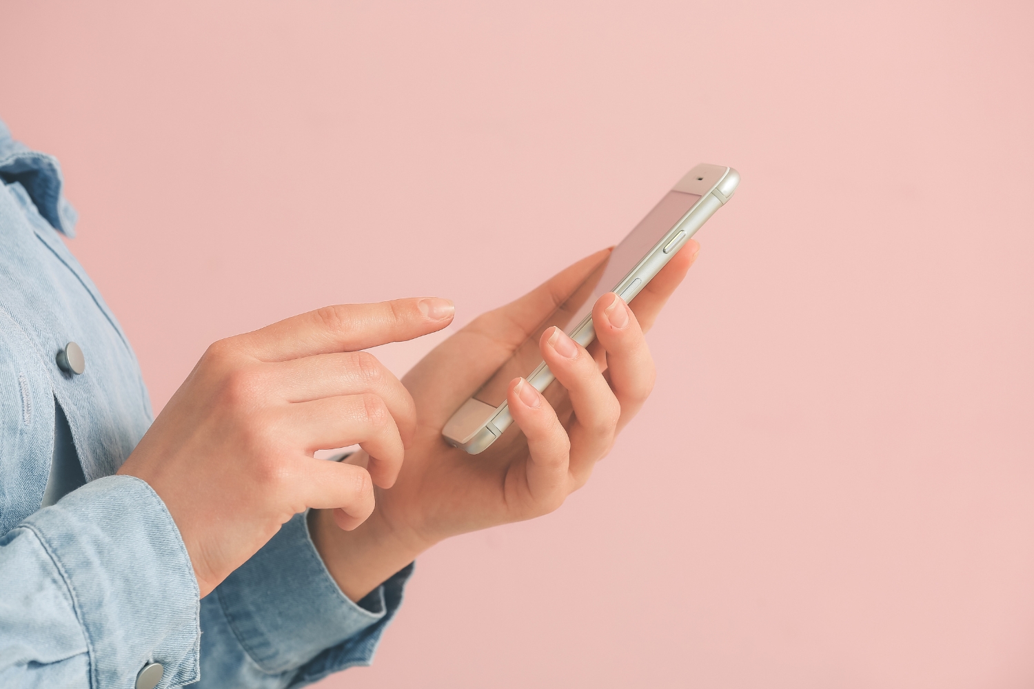 Rózsaszín háttér, nő keze, a telefonját nyomkodja