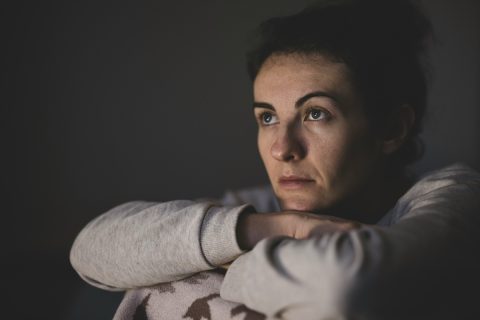 szürke melegítős nő felhúzott lábbal, kezeit maga előtt keresztbe teszi és felnéz