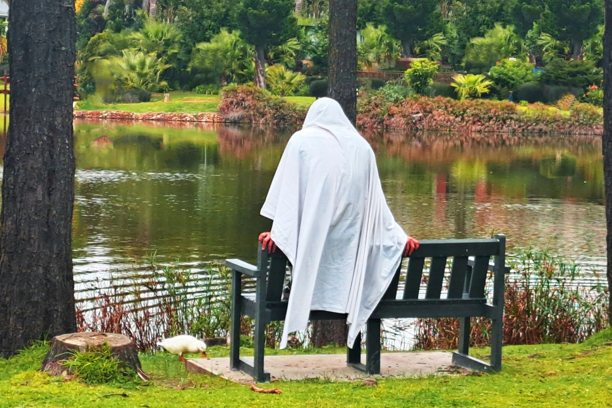 Szellemnek öltözött férfi ül egy park padján