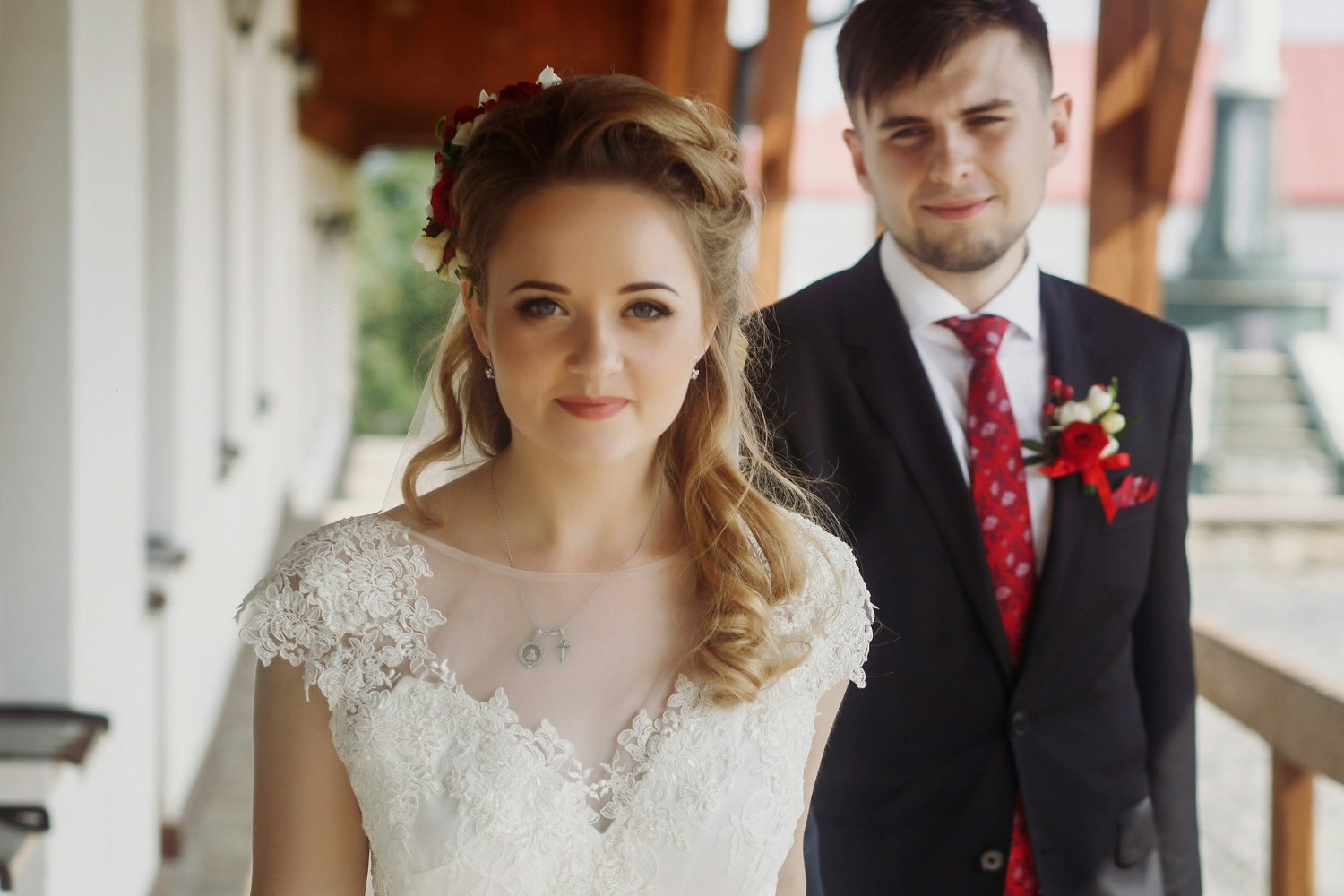 Férj és feleség esküvői ruhában, a nő megy elöl a kamerába nézve
