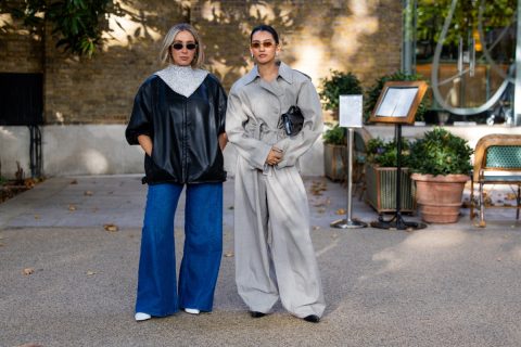 Két vendég a Barbour bemutatója előtt a londoni divathéten: az egyik fekete bőrdzsekiben, ezüst díszítésű, magas nyakú felsőben és bő szárú farmerben, a másik világosszürke trencskabátban, hozzá illő bő szárú nadrágban és fekete borítéktáskával.