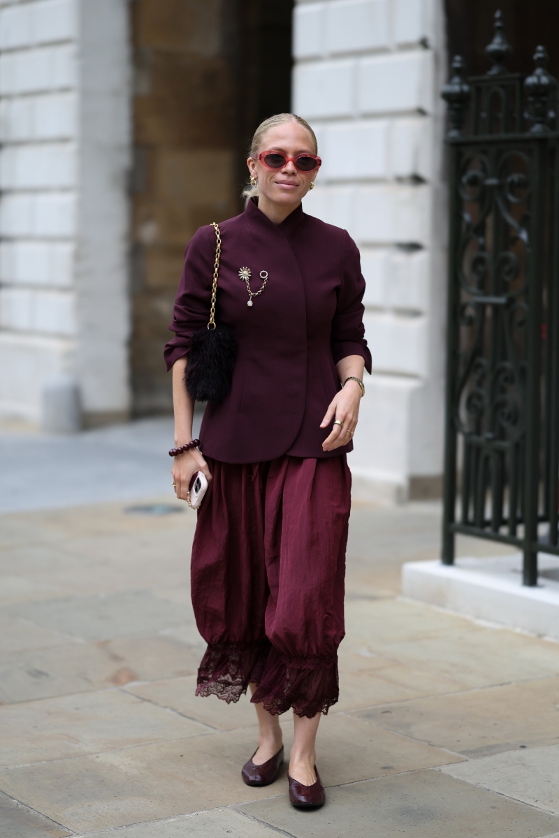 londoni-divathet-2026-streetstyle-ezt-viseljuk-osszel | Marie Claire Vendég bordó, magas nyakú, átlapolt fazonú zakóban, hozzá illő bő, rövidített, csipkeszegélyes nadrágban, bordó szögletes orrú balerinacipőben, arany láncos fekete szőrmetáskával és piros lencsés napszemüvegben a Dreaming Eli bemutatója előtt a londoni divathéten.