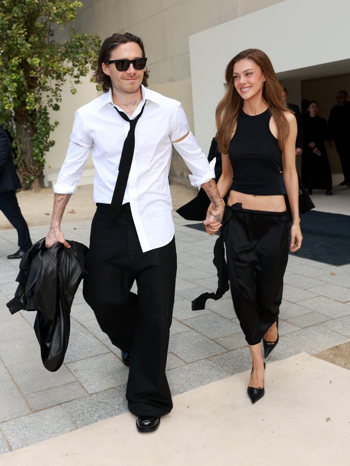 Brooklyn Beckham félrecsúszott nyakkendőben és fehér ingben és Nicola Peltz fekete felsőben és szoknyában
