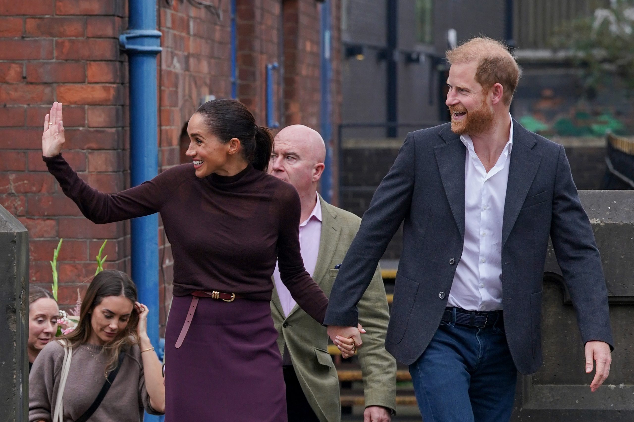 meghan-markle-apja-botrany-menekul | Marie Claire Meghan Markle és Harry herceg emberek között, Meghan bordó ruhában integet