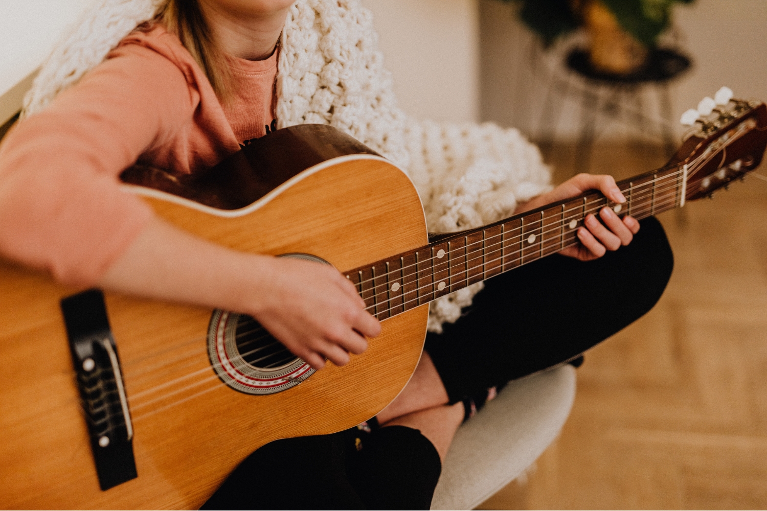 1. Zenélés | Marie Claire Nő gitározik széken ülve, vállán fehér kötött takaró