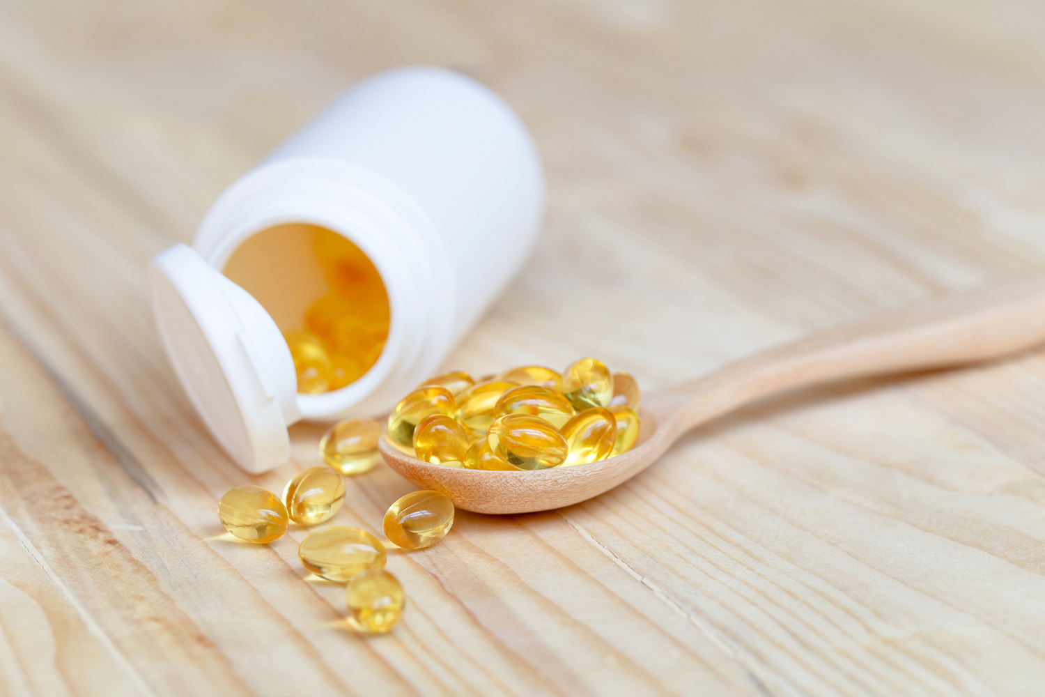 D-vitamin kapszulák egy kanálon és mögötte egy fehér dobozban