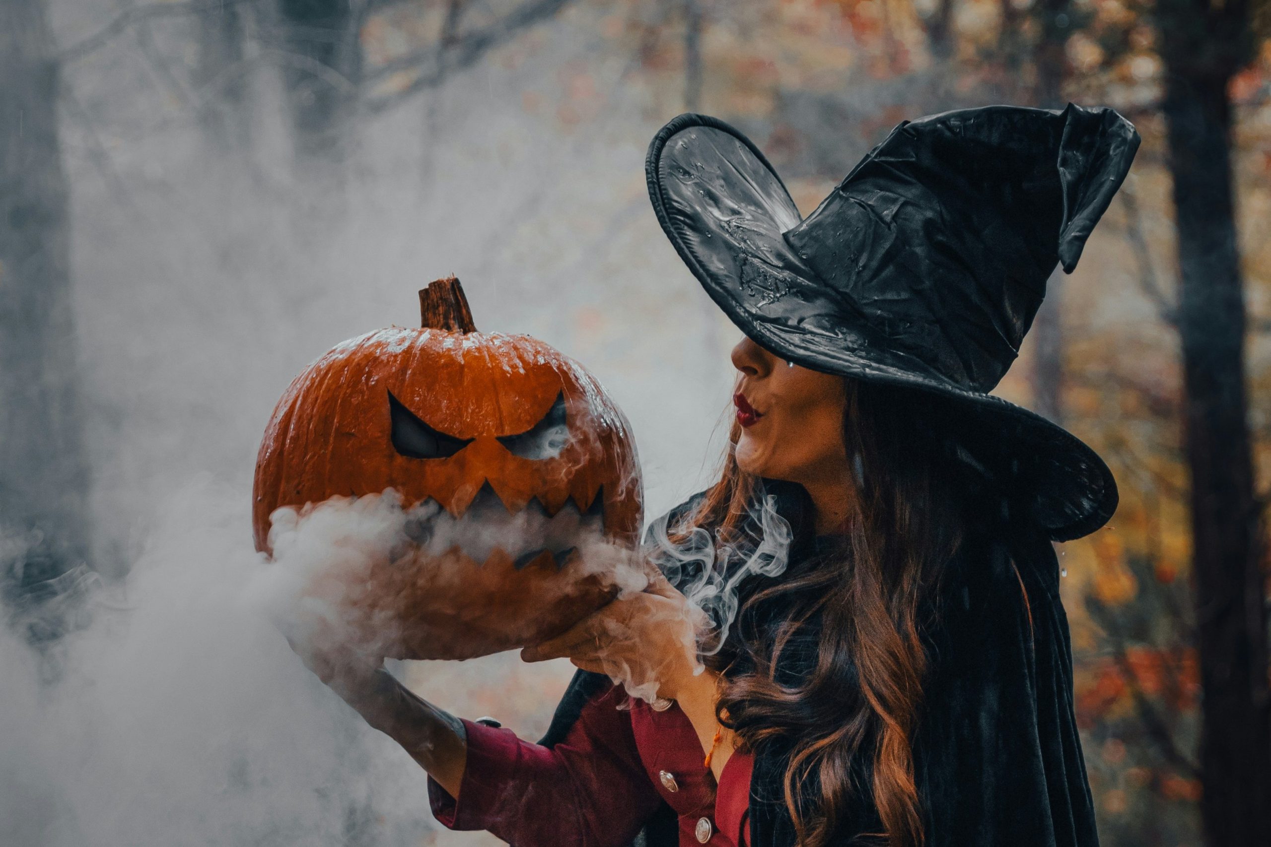 boszorkánykalapot viselő nő halloweeni tökre fúj rá, amelyből füst száll ki