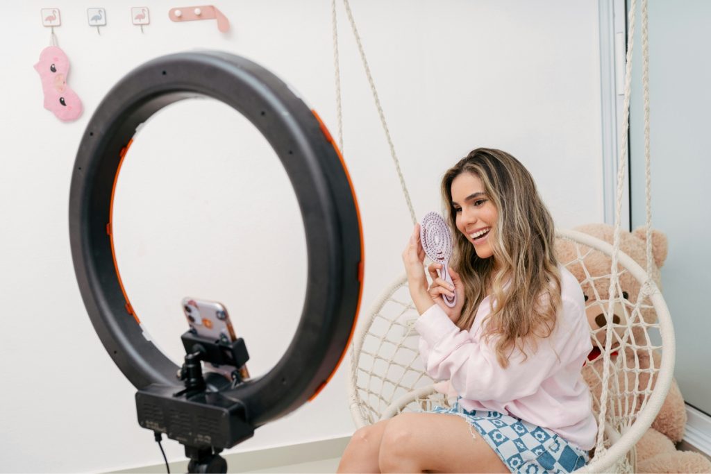 tiktok-beauty-trendek-z-generacio2 | Marie Claire influenszerlány ül egy hintában, fésűt mutat, előtérben körvaku